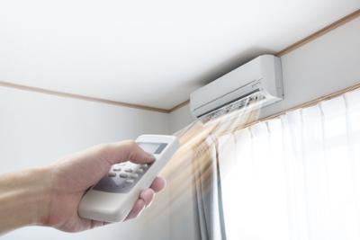 One hand operates the remote control of an air-conditioning unit.