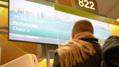 hombre de espaldas en el aeropuerto visualizando pantalla de facturación para el destino doha