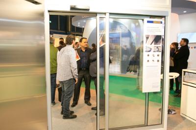 Uno de los stands de SMART DOORS en el que se ve una puerta automática de cristal y varios profesionales